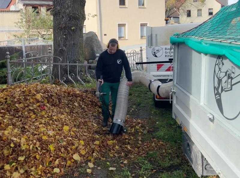 Laubbeseitigung mit Laubsauger am Firmenfahrzeug auf Gehweg